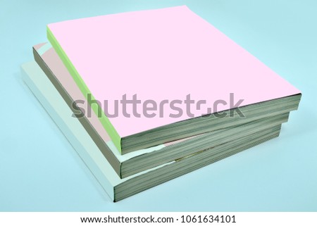 Stack of three thick magazines or books, catalogs with a blank pink soft cover on a blue background - a mock up for demonstrating your design