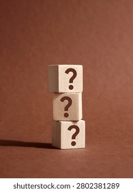 Stack of three wooden cubes with question marks on brown background representing frequently asked questions, problem solving and business solution
