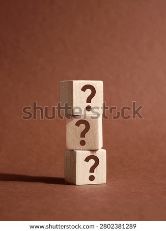 Stack of three wooden cubes with question marks on brown background representing frequently asked questions, problem solving and business solution