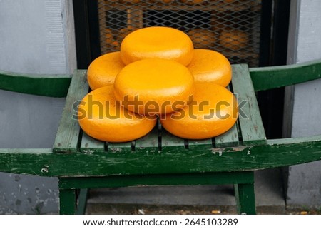 A stack of traditional Gouda cheese wheels with yellow-orange rinds, displayed on a wooden stand