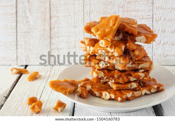 Stack of traditional peanut brittle candy\
pieces against a white wood\
background
