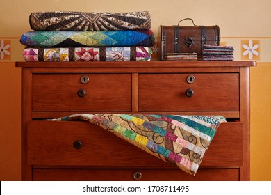 Stack Of Traditional Quilts And Wooden Chest On Chest Of Drawers