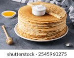 Stack of traditional russian pancakes blini with honey and sour cream on gray background