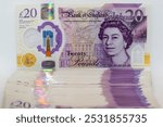 A stack of twenty pound banknotes from the Bank of England featuring Queen Elizabeth II. The banknotes are arranged vertically, with the top bill fully visible. The image is taken against a white back