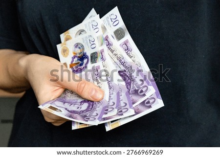 A stack of twenty pound banknotes from the Bank of England featuring Queen Elizabeth II in hands of a woman