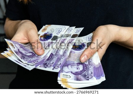 A stack of twenty pound banknotes from the Bank of England featuring Queen Elizabeth II in hands of a woman