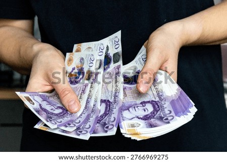 A stack of twenty pound banknotes from the Bank of England featuring Queen Elizabeth II in hands of a woman