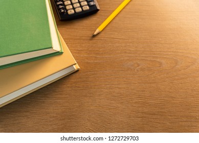 stack of two aged books sitting on a wooden brown table with calculator and pencil