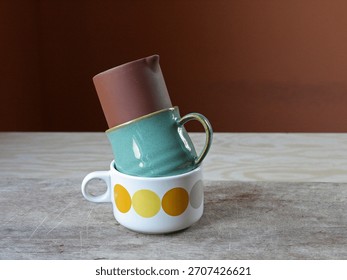 A stack of two ceramic mugs and of one ceramic creamer on a wooden surface
