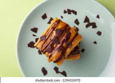 Stack Of Two Sweet Potato Blondies, Thin Lines Of Chocolate And Caramel Icing Running Down On The Sides, Chocolate Chips, Teal Plate, Green Background, Top Down View, Landscape Orientation