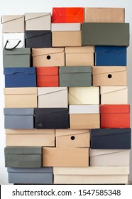 Stack Of Unevenly Folded Shoe Boxes Against A White Wall. Seasonal Sales And Discounts. Vertical Photo.

