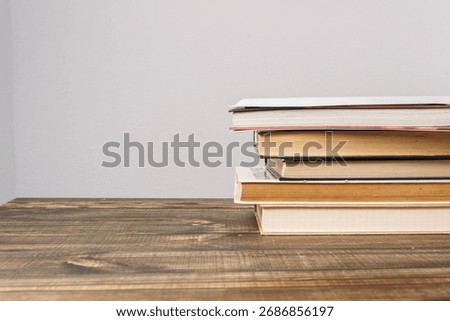 A stack of various books rests on a wooden table, representing the pursuit of knowledge and education in a cozy setting