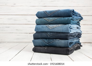 Stack Of Various Denim Jeans, Trousers On Wooden Rustic Background, Fashion Design 