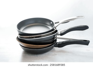 Stack of various frying pans made from cast iron, carbon steel, non-stick coated and stainless steel, choosing the right kitchen ware, light gray background, copy space, selected focus