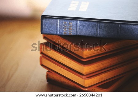 Stack of vintage Bibles with a close-up focus on the spine of a blue Holy Bible on top. Represents religious study, Christian faith, scripture preservation, and spiritual tradition.