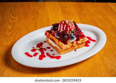 A stack of waffles topped with berries, creamy ice cream, and a drizzle of sauce.