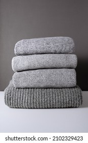 stack of warm grey knit sweaters on white table and gray background. Cold autumn season texture detail