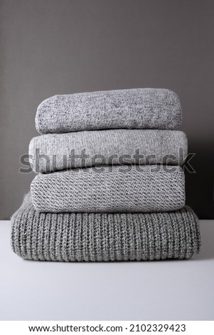 stack of warm grey knit sweaters on white table and gray background. Cold autumn season texture detail