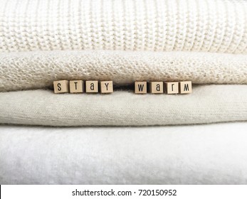 Stack Of Warm White Knitted Things With Words Stay Warm