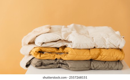 Stack of warm winter jackets in various colors, creating a cozy and inviting scene for autumn and winter fashion