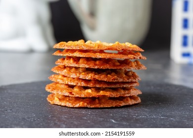 Stack of waver-thin Dutch sugar and butter cookies (kletskoppen) with almonds, on dark table. Natural light, selective focus. 