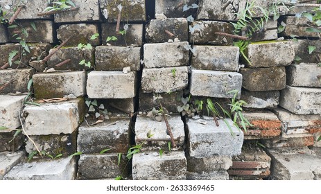 A stack of weathered concrete blocks and bricks, overgrown with moss and small plants. Ideal for rustic landscaping, demolition debris, or textured background.