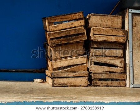 A stack of weathered wooden fruit crates against a vibrant blue wall, perfect for rustic concepts.