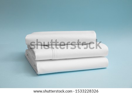 Stack of white bedding against blue backdrop, folded soft bed clothes, stack of white cotton sheets on a blue background for advertising, commercial and mock up