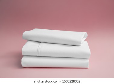 Stack Of White Bedding Against Pink Backdrop, Folded Soft Bed Clothes, Stack Of White Cotton Sheets On A Pink Background For Advertising, Commercial And Mock Up