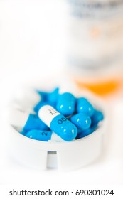 Stack of white and blue pills or capsules in the white cap of an orange prescription bottle