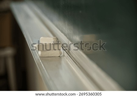 A stack of white chalk erasers rests on the ledge of a chalkboard, reflecting light and shadow.