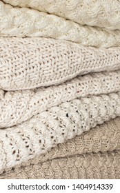 Stack of white cozy knitted sweaters. Knitted background, texture, pattern. Closeup of sample with knitting weave. 