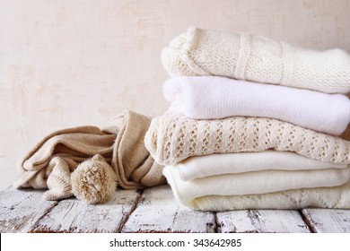 Stack of white cozy knitted sweaters on a wooden table
