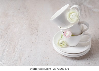 Stack of white cups, plates and beautiful flowers on light textured table, closeup. Space for text
