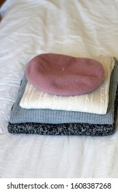Stack of white, gray and black sweaters with pink beret. Selective focus.