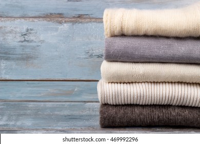 Stack of white and gray cozy knitted sweaters on rustic wooden background