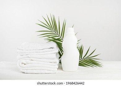 A stack of white linen and a bottle of white palm-leafed laundry detergent or fabric softener. Tropical Laundry Day Mockup.