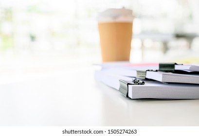 Stack of white paper with black clips clamped and cup of coffee on white table, focus on paper, shalow DOF.