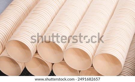 A stack of white paper cups are on a table. The cups are all the same size and shape