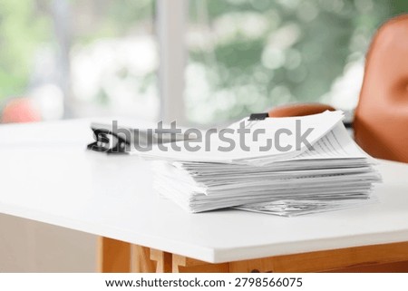 Stack of white paper documents on a clean office desk with a hole puncher and binder clip, business administration and organization