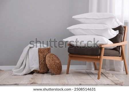 Stack of white pillows, armchair and wicker basket on floor indoors