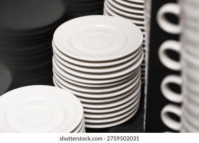 Stack of white plates and cups in restaurant kitchen. Catering and gastronomy equipment concept. Clean dishware arrangement for food service business and organized hospitality workspace use.