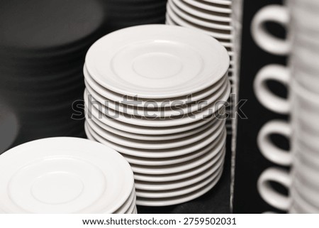 Stack of white plates and cups in restaurant kitchen. Catering and gastronomy equipment concept. Clean dishware arrangement for food service business and organized hospitality workspace use.