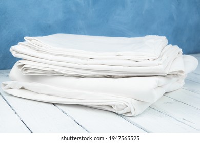 Stack Of White Sheets On Wooden Table. Folded Fabric. Clean And Ironed Tablecloths. Bed Linen Is Washed And Prepared For Guest