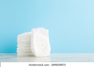 Stack of white soft new baby diapers on wooden table at light blue wall background. Pastel color. Closeup. Empty place for text or logo.