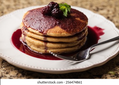 Stack of whole grain white wheat pancakes with homemade boysenberry syrup and a glass of milk on granite counter top view from top