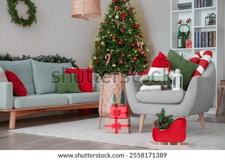 Stack of winter clothes with Christmas decorations and gift boxes on armchair at home