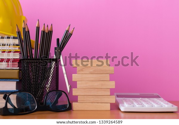 Stack\
wooden blocks with pencils, dividers, glasses, construction helmet,\
calculator and stack of book on wooden table isolated pick\
background, Blank wooden blocks for your\
text.