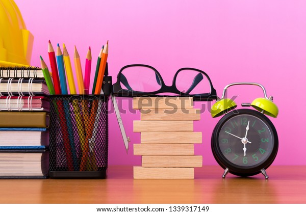 Stack wooden blocks\
with pencils, dividers, glasses, construction helmet, clock and\
stack of book on wooden table isolated pick background, Blank\
wooden blocks for your\
text.