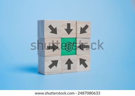 A stack of wooden blocks with various arrows pointing towards a target center on a blue background. Target, objective and direction concept.